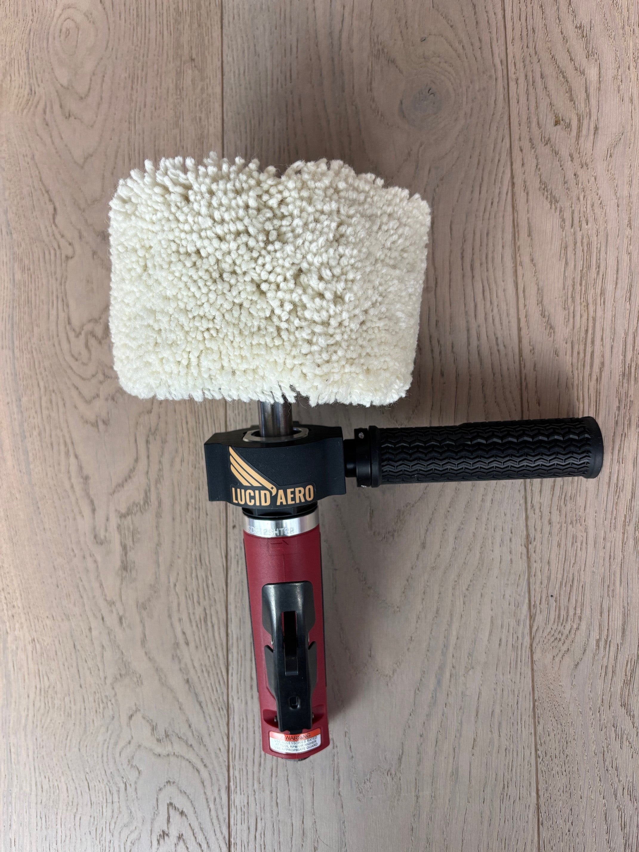 Lucid Aero Compact Drum Buffer overhead view on wood surface, wool sleeve installed, handle extending right