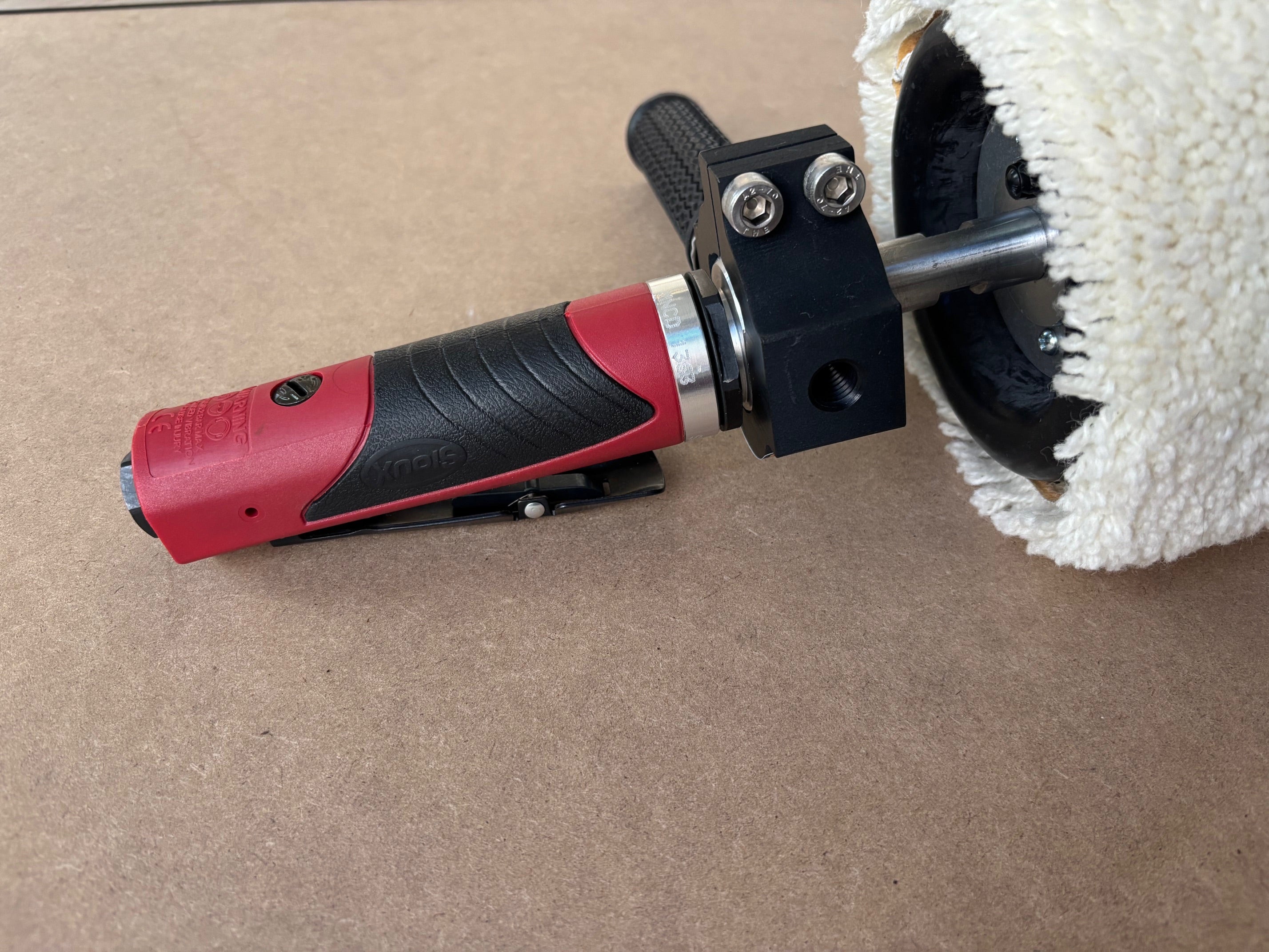 Lucid Aero drum buffer side profile showing red pneumatic motor body, throttle trigger, anodized clamp, and wool sleeve